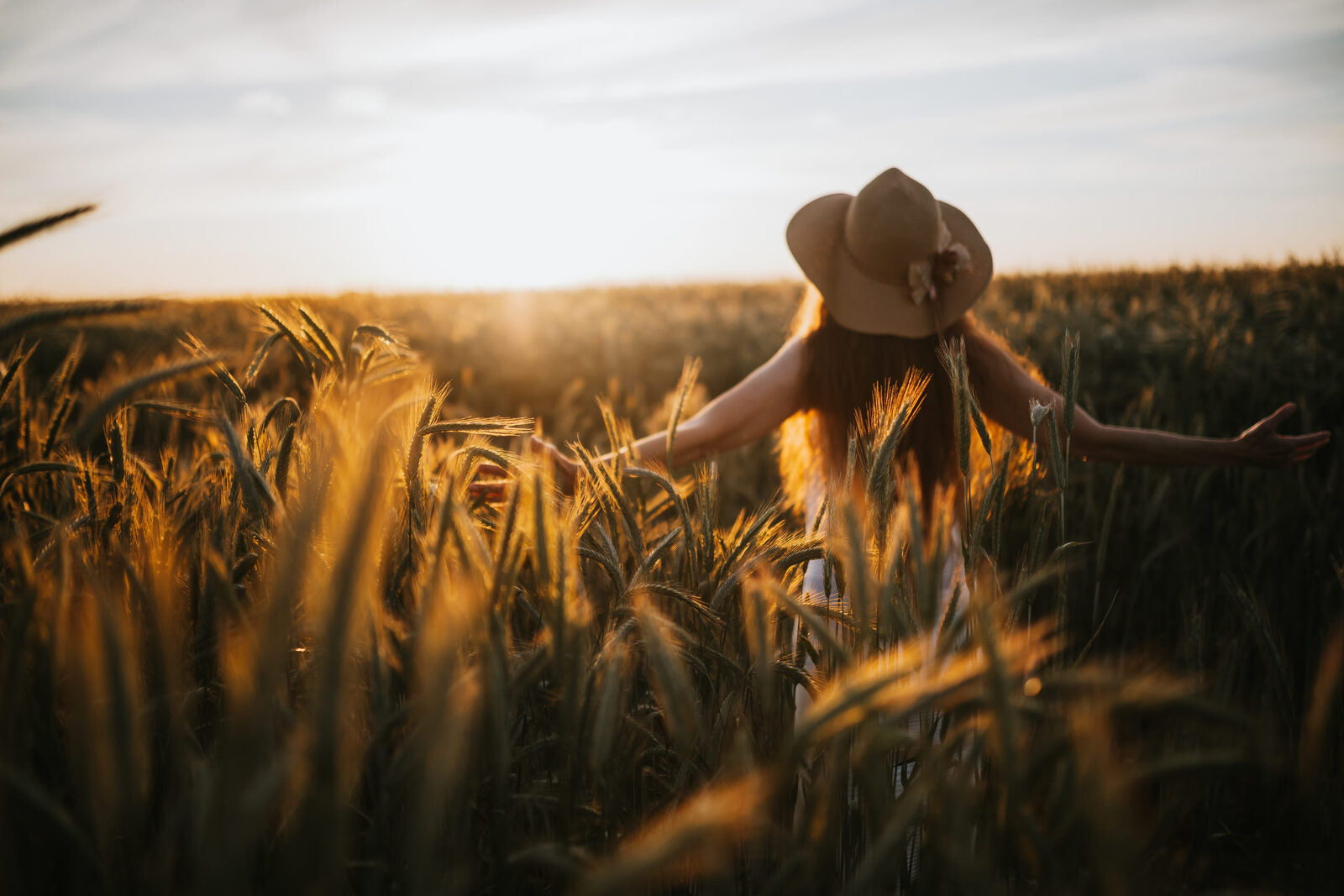 Frau steht im goldenen Getreidefeld im Abendlicht und breitet die Arme aus – natürliches Wohlbefinden und Freiheit.